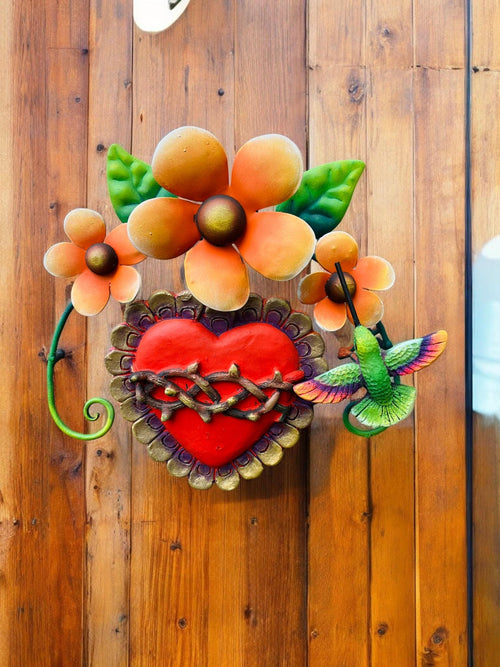 Handmade Mexican metal heart with hummingbird displayed outdoors, colorful folk art