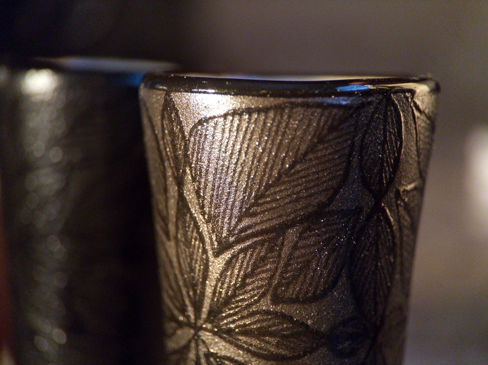 Detail of a carved leaf-pattern shot glass from the black stoneware skull decanter set, handmade in Mexico