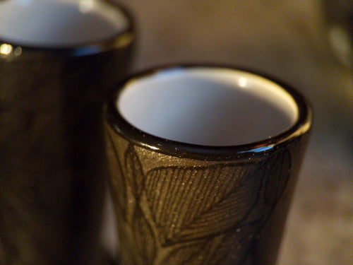 Close-up of a black stoneware shot glass with carved pattern from the handmade Mexican skull decanter set