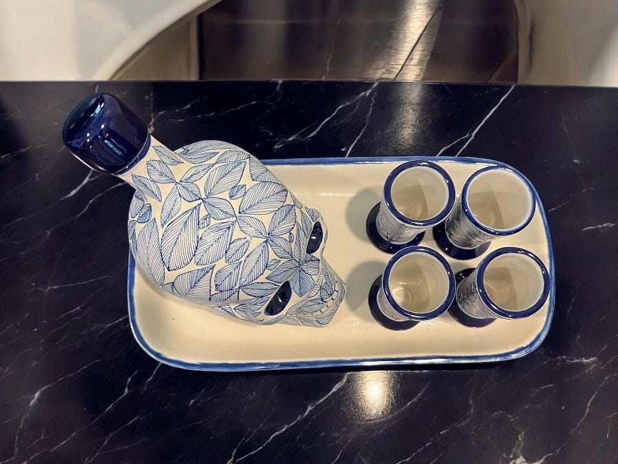Blue Mexican skull decanter with four shot glasses arranged on dark marble, handmade Day of the Dead tequila set