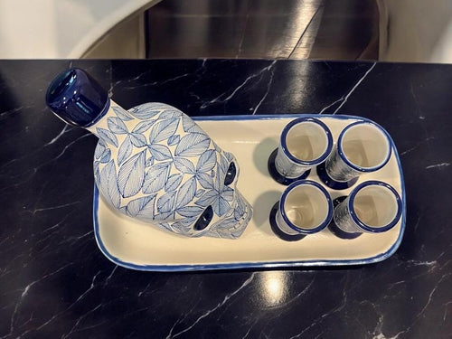Blue Mexican skull decanter with four shot glasses arranged on dark marble, handmade Day of the Dead tequila set