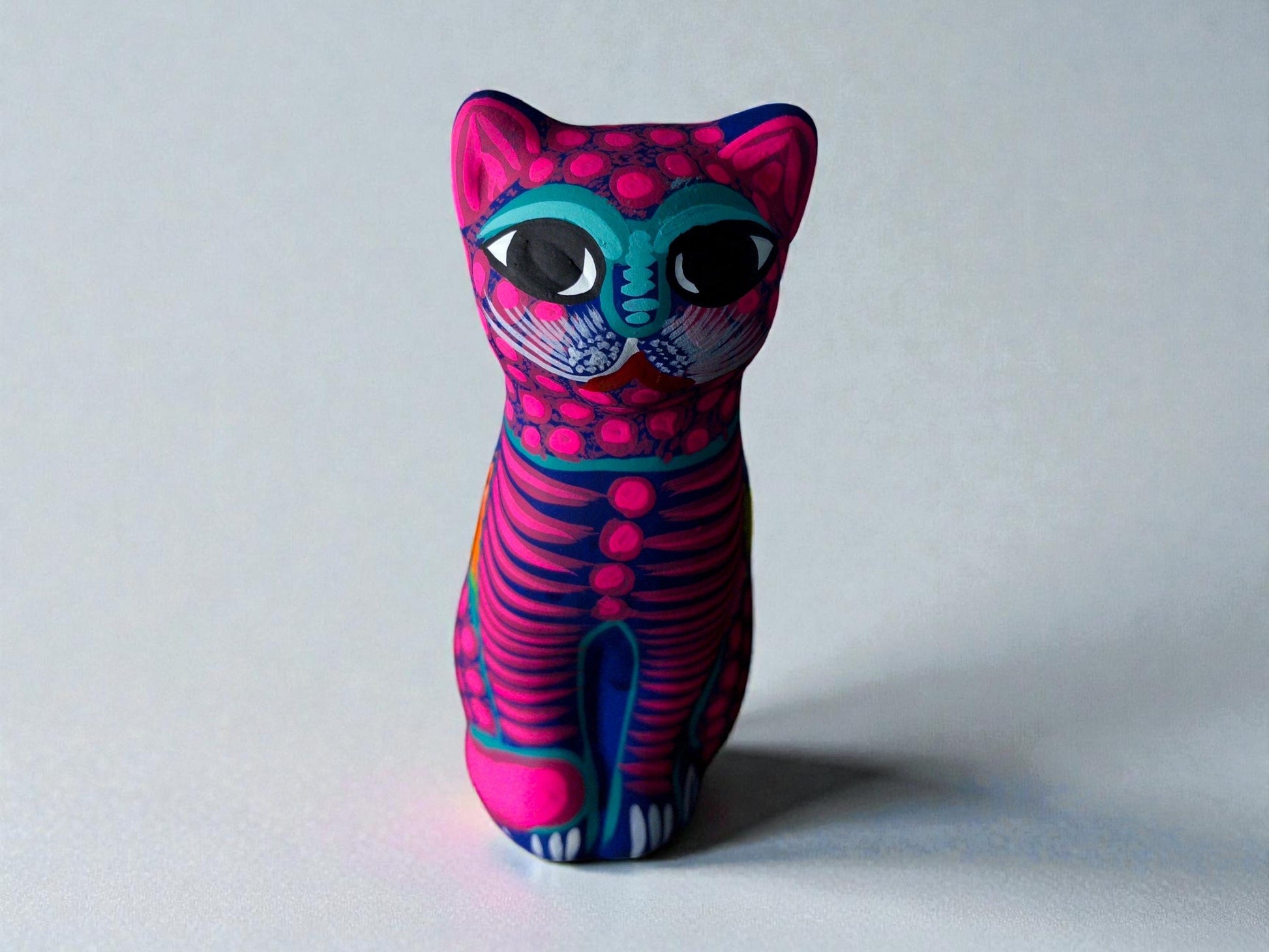 Pink clay cat alebrije with teal eyes and floral details, handmade Mexican folk art figurine